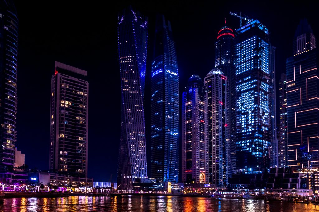 Illuminated skyscrapers of Dubai Marina at night, reflecting on the water.