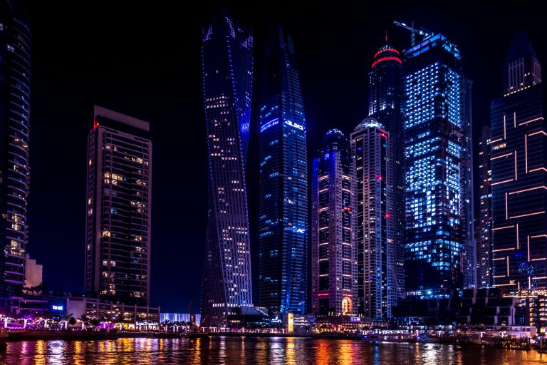 Illuminated skyscrapers of Dubai Marina at night, reflecting on the water.